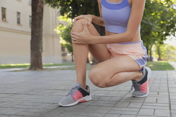 スポーツウェアを着た若い女性が街の通りで膝の問題を抱えて — ストック写真