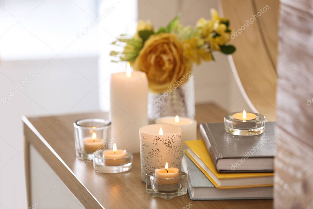 Beautiful burning candles, books and flowers on table at home