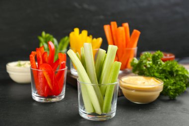 Kereviz ve diğer sebze çubukları cam kaselerde sos sosu siyah masada.