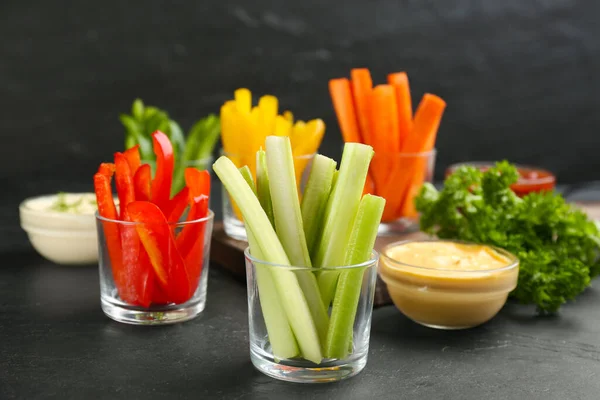 Celery and other vegetable sticks in glass bowls with dip sauce on black table