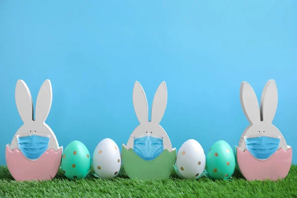 Covid 19大流行病 复活节兔子形象 戴着防护面具 在浅蓝色背景的绿草上涂上彩蛋 — 图库照片