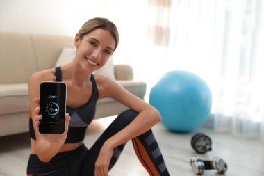 Akıllı telefonu olan genç bir kadın. Kapalı alanda fitness uygulaması var. Cihaza odaklan.