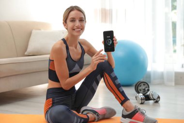 Genç kadın akıllı telefonu evde fitness uygulaması ile gösteriyor