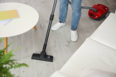 Evde elektrikli süpürge kullanan genç adam, yakın plan.