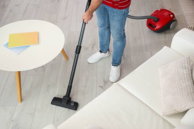 Evde elektrikli süpürge kullanan genç adam, yakın plan.