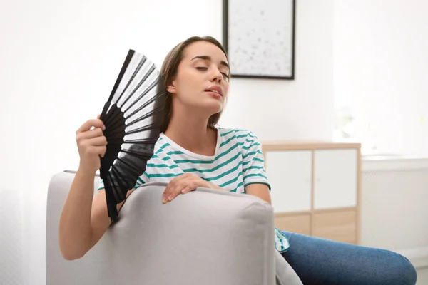 Woman enjoying air flow from hand fan at home. Summer heat