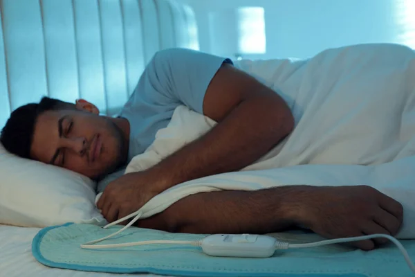 Man sleeping on electric heating pad in bed at night