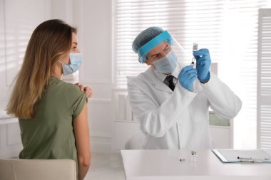 Doktor şırıngayı Covid-19 'a karşı aşıyla doldururken hasta klinikte iğne olmayı bekliyor.