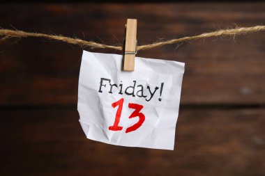Crumpled paper note with phrase Friday! 13 hanging on twine against wooden background. Bad luck superstition clipart