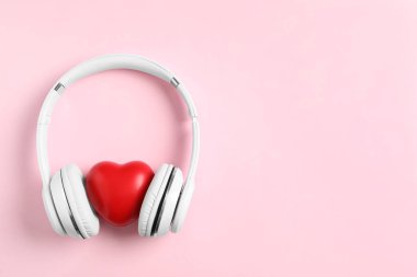 Modern kulaklıklar ve pembe arka planda kırmızı kalp, yazı için yeri olan düz bir yer. Aşk şarkıları dinlerken
