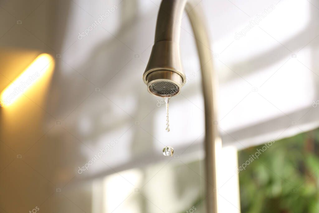 Water drops falling down from tap on blurred background, closeup