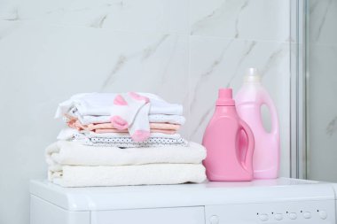Banyodaki çamaşır makinesinde bir şişe deterjan ve çocuk kıyafetleri.
