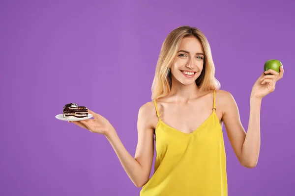 紫の背景にケーキと健康的なリンゴの間で選択する女性 — ストック写真