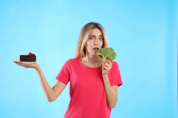 Mujer Eligiendo Entre Pastel Brócoli Saludable Sobre Fondo Azul Claro —  Fotos de Stock