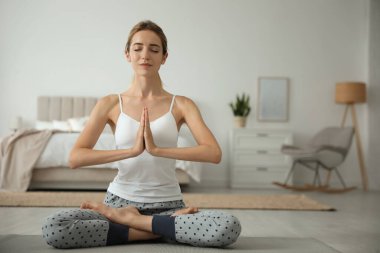 Genç bir kadın evde yerde meditasyon yapıyor. Sabah sporu