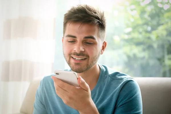 Young man using voice search on smartphone indoors