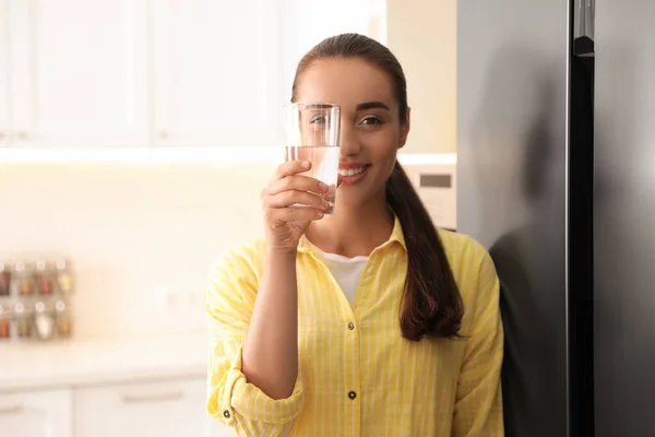 Young woman looking through glass of pure water in kitchen