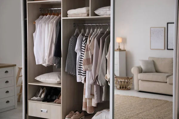 Wardrobe closet with different stylish clothes, shoes and home stuff in room