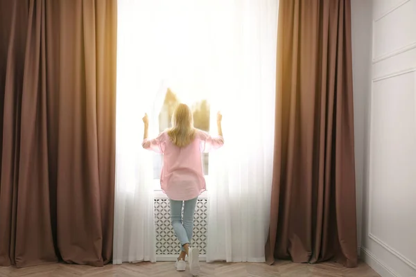 Young Woman Opening Window Curtains Home Back View — Stock Photo, Image