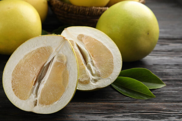 Fresh cut and whole pomelo fruits on black wooden table, closeup
