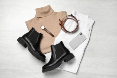 Şık botlar, yeni elbiseler, akıllı telefon ve beyaz ahşap arka planda aksesuarlar, düz yatış.