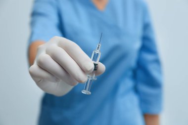 Doktor elinde COVID-19 aşısı olan şırıngayı arka planda tutuyor.