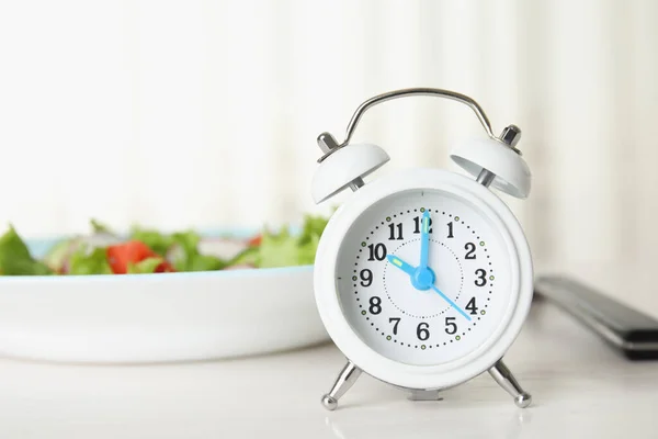 白いテーブルの上にサラダ付き目覚まし時計とプレート 食事のタイミングのコンセプト — ストック写真