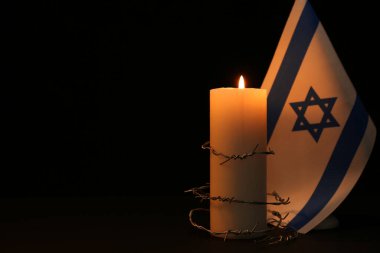 Flag of Israel, barbed wire and burning candle on black background, space for text. Holocaust memory day clipart