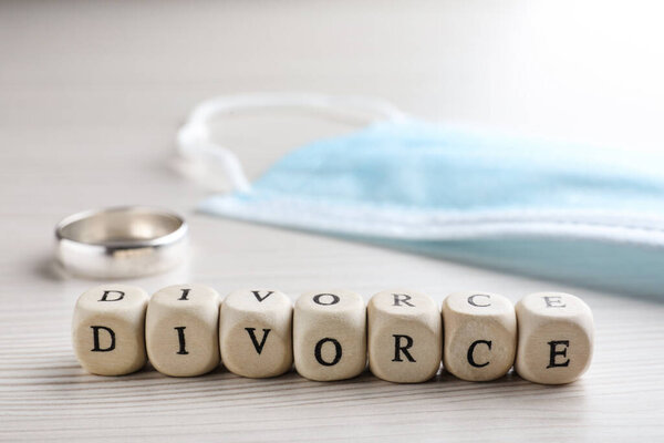 Cubes with word Divorce, protective mask and wedding ring on white wooden table, closeup