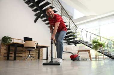 Genç adam oturma odasında elektrikli süpürge kullanıyor.