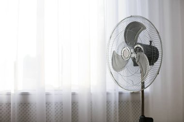 Pencerenin yanındaki modern elektrikli vantilatör. Metin için boşluk
