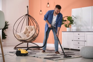 Evde elektrikli süpürge kullanan genç bir adam.