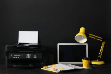 Siyah arka planda modern yazıcı, dizüstü bilgisayar ve ofis malzemeleri