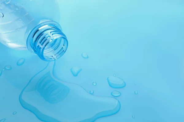 Drops of spilled water and plastic bottle on light blue background, closeup