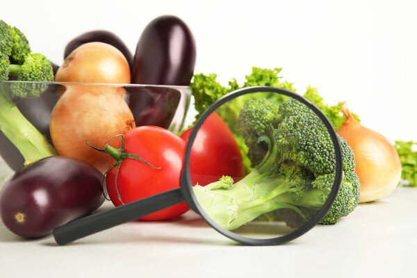 Different fresh vegetables and magnifying glass on table, closeup. Poison detection