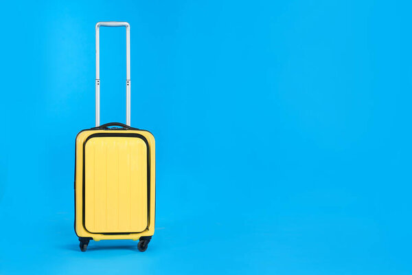 Yellow travel suitcase on light blue background, space for text. Summer vacation