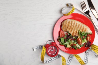İştah açıcı yemek ve alarm saatiyle bembeyaz ahşap masa üzerinde düz kompozisyon, yazı için boşluk. Beslenme rejimi