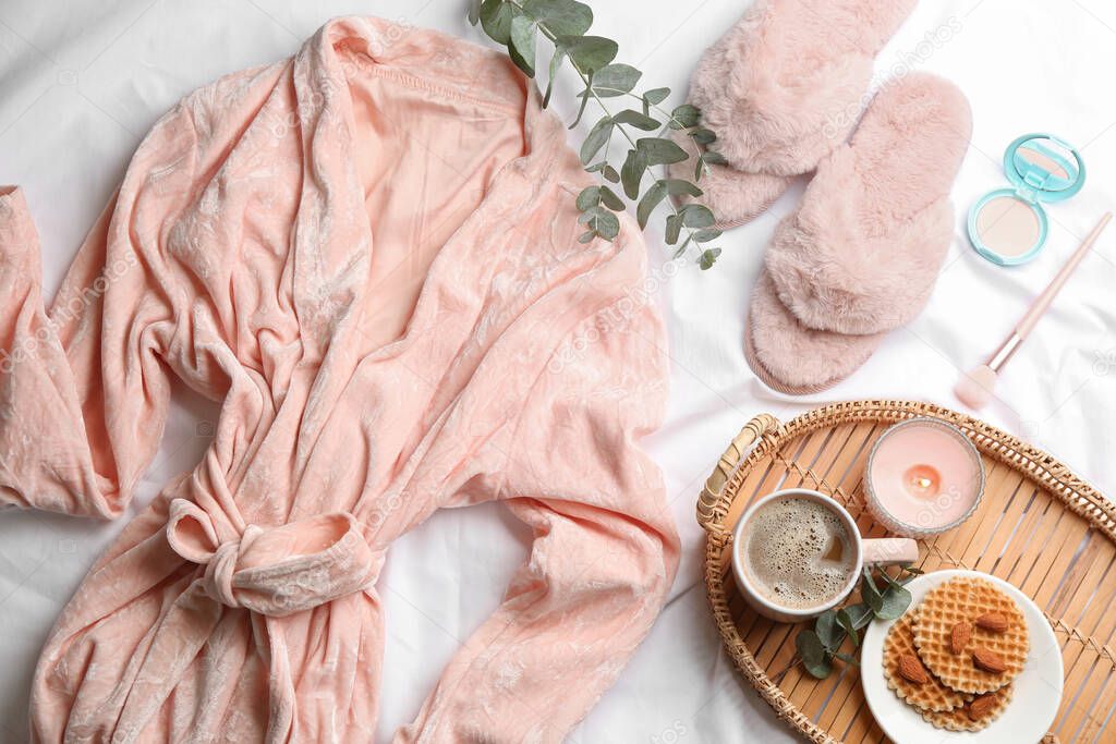 Flat lay composition with fluffy slippers and bath robe on white bedsheet. Comfortable home outfit