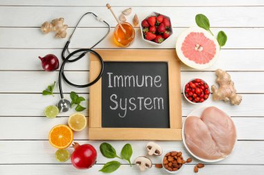 Beyaz ahşap masa üzerinde bağışıklık sistemi, steteskop ve taze ürünler içeren tebeşir tahtası, düz konum