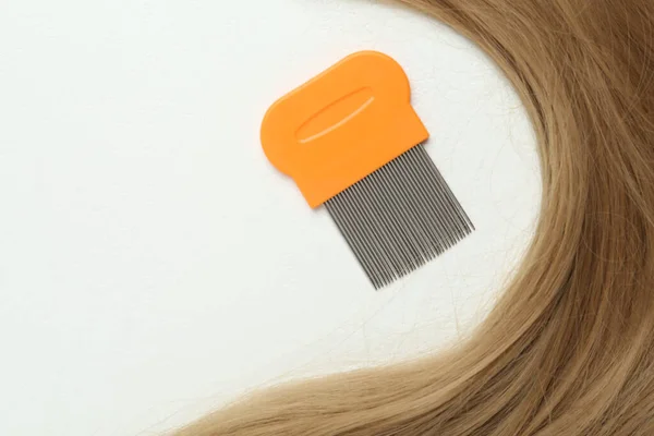 Metal comb and blond hair on white background, flat lay. Anti lice treatment