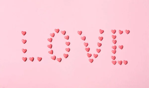 Słowo Miłość Wykonana Posypki Kształcie Serca Różowym Tle Płaski Leżak — Zdjęcie stockowe