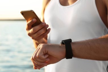 Fitness izleyicisi ve akıllı telefonu olan bir adam nehir kenarındaki eğitimden sonra sonuçları kontrol ediyor.