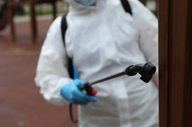 Çocuk parkında kimyasal koruyucu elbise giyen kadın dezenfektan spreyine odaklan. Koronavirüs salgını sırasında önleyici önlemler