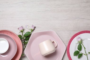 Beyaz ahşap masa üzerinde güzel bulaşık takımları ve güllerle bezenmiş düz bir kompozisyon. Metin için boşluk