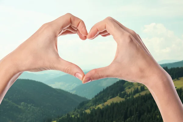 Woman making heart with hands in mountains on sunny day, closeup