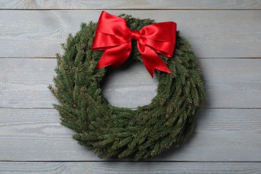 Noel çelengi, gri ahşap arka planda kırmızı fiyonklu köknar dallarından yapılmıştır.