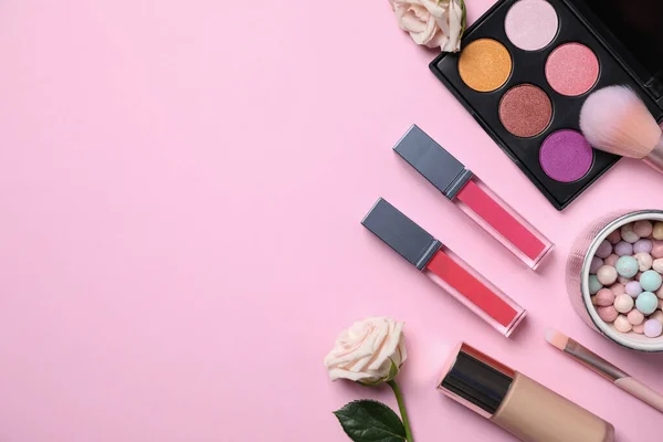 Flat lay composition with makeup products and roses on pink background, space for text