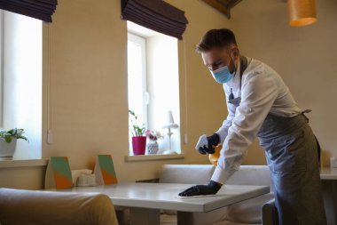 Garson, restoranda paçavra ve deterjanla masayı temizliyor. Koronavirüs karantinası sırasında yüzey tedavisi
