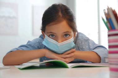 Uzaktan öğrenme, Covid-19 salgını yüzünden evde online çalışma. Koruyucu maskeli kız odada ödev yapıyor.