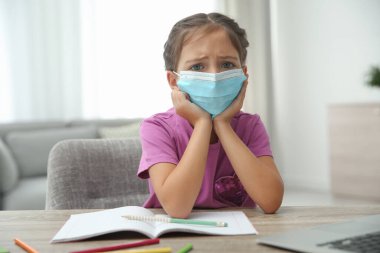 Uzaktan öğrenme, Covid-19 salgını yüzünden evde online çalışma. Koruyucu maskeli kız odada ödev yapıyor.